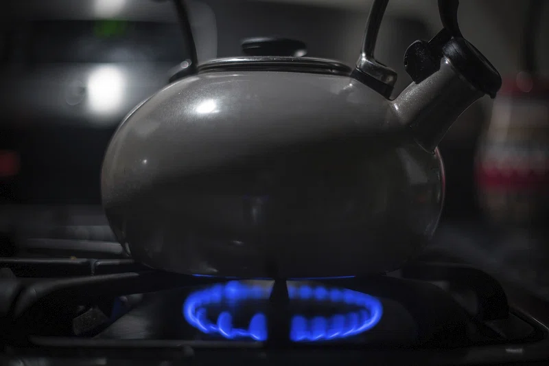 Closeup grey scale picture of a kettle on a gas stove with a bright blue gas flame